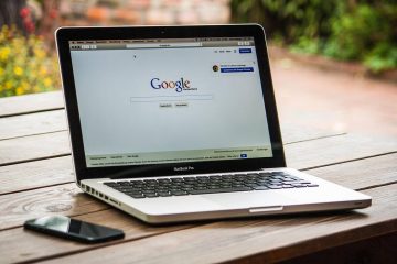 Laptop ouvert sur Google, smartphone à gauche, table en bois, jardin flou